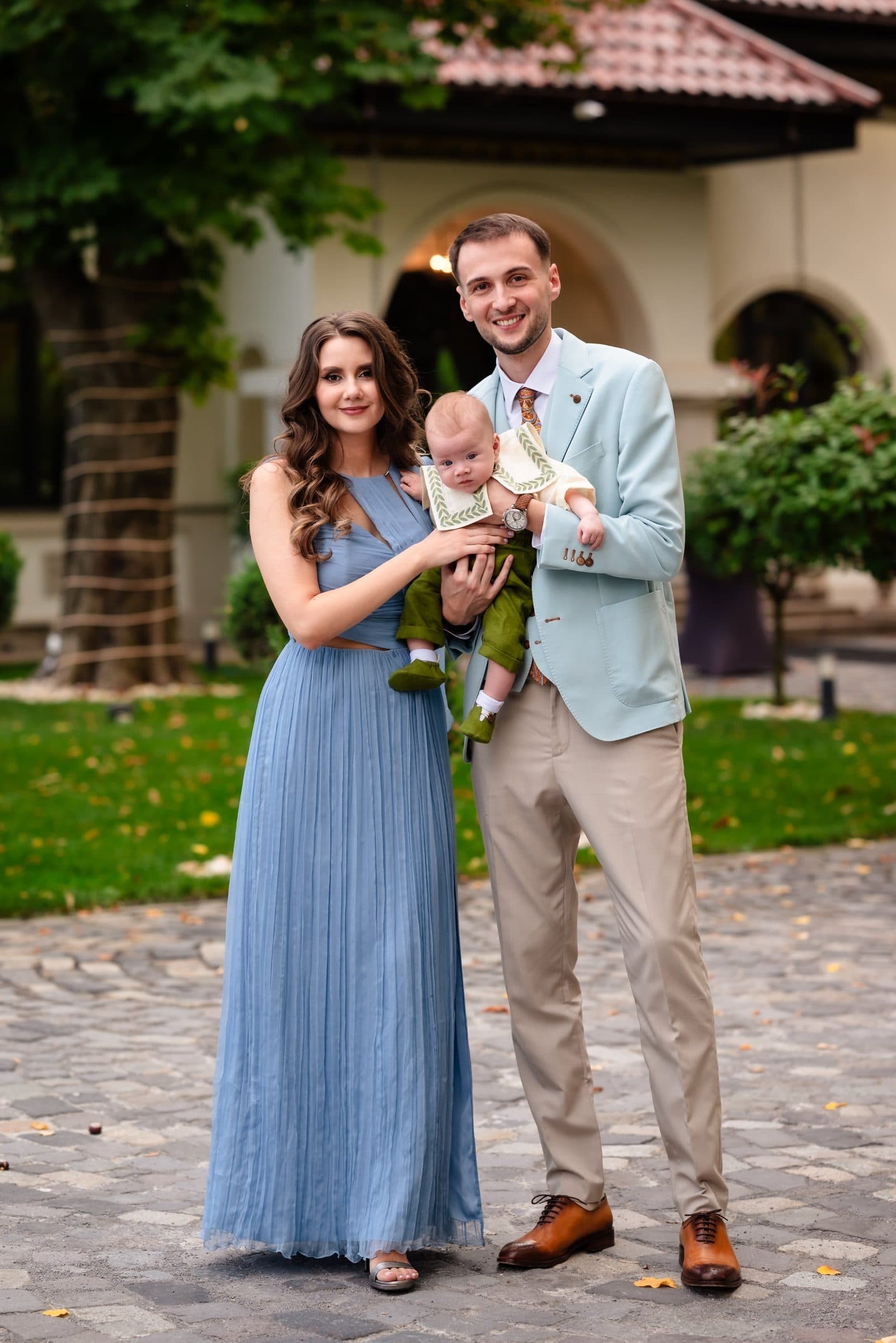 Parents holding their baby in front of an arched villa
