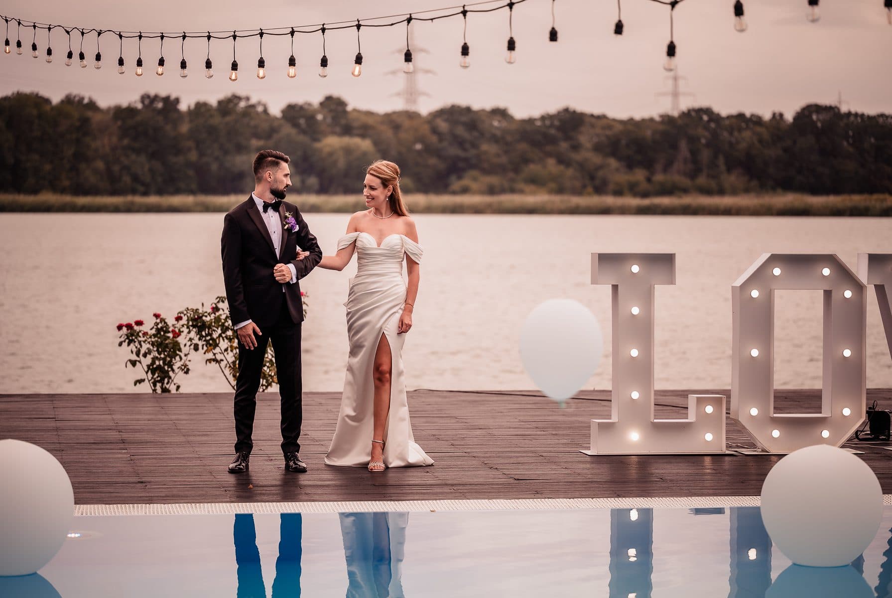 The bride and groom walk along the deck past glowing LOVE letters