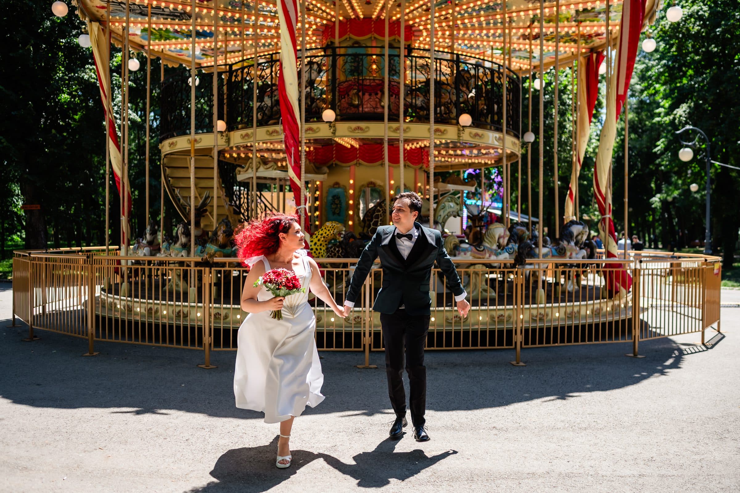 Bride and groom stride toward the camera, laughing, in front of the carousel
