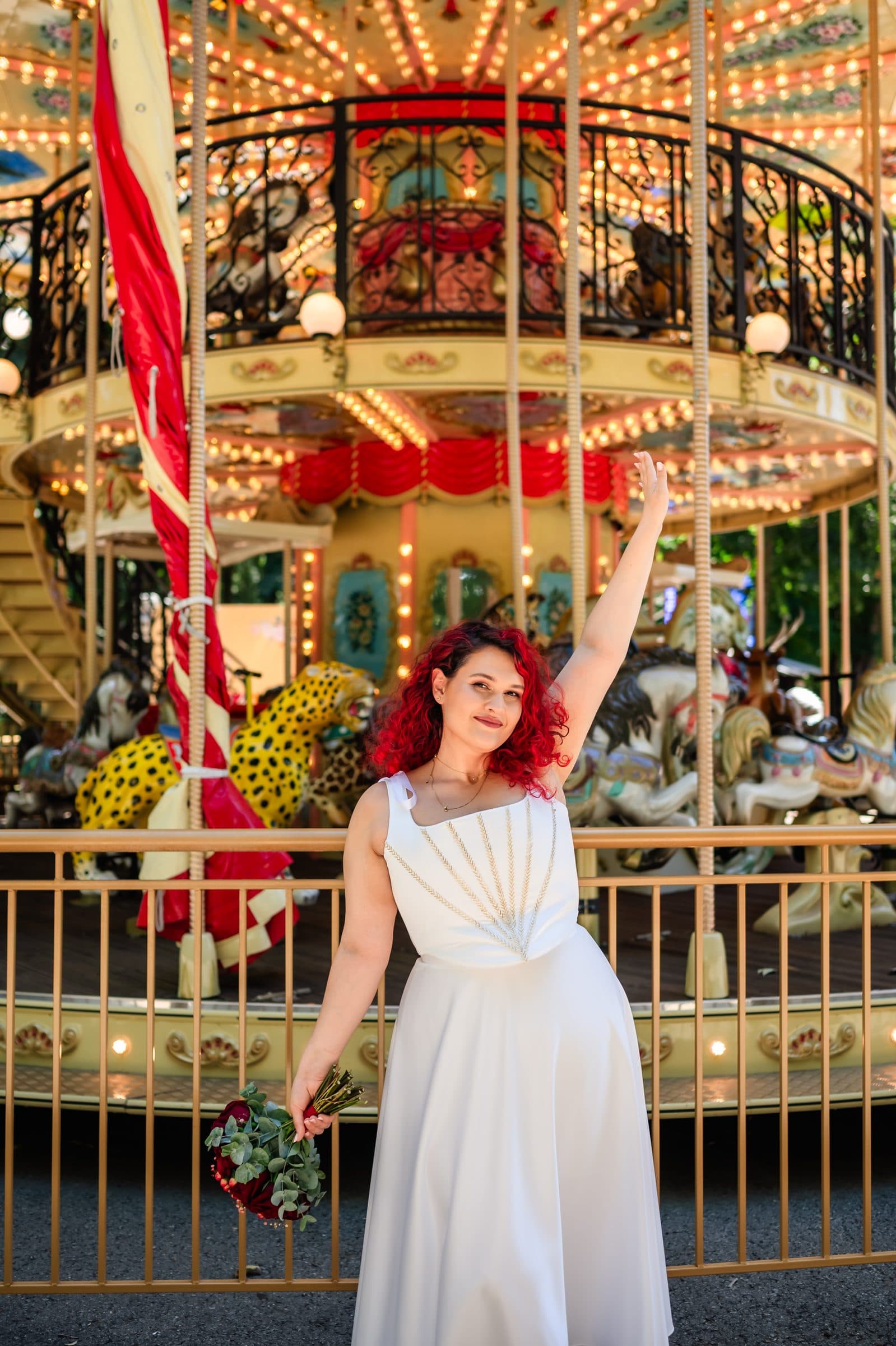 The bride throws one arm up in front of the lit carousel