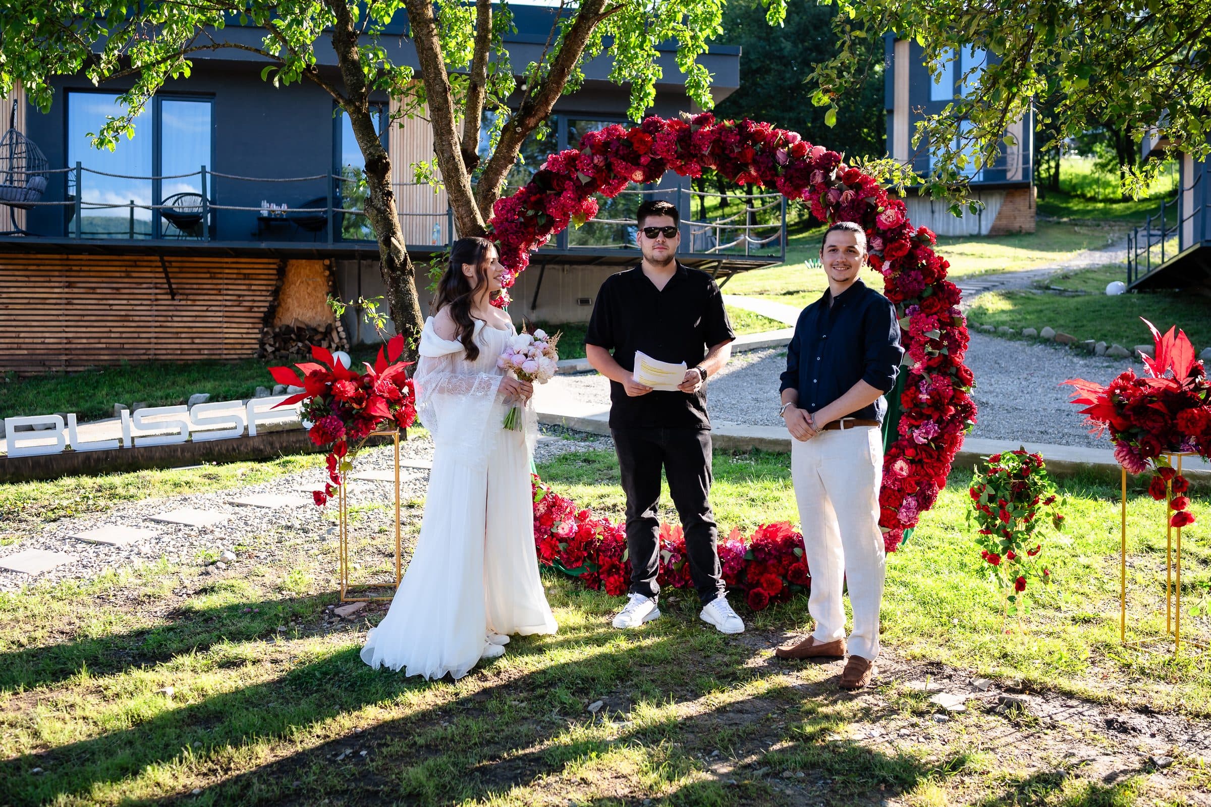 Bride and groom under a ring of red flowers during an outdoor ceremony