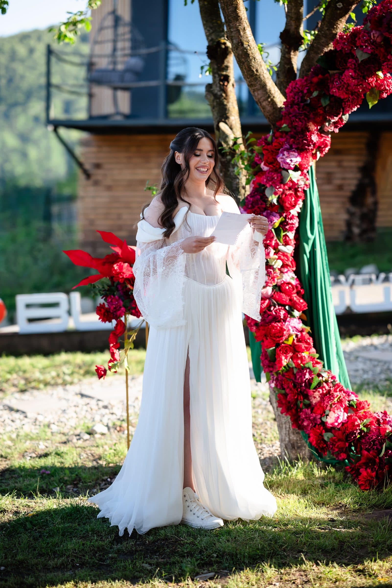 The bride reads her vows beside the red flower arch