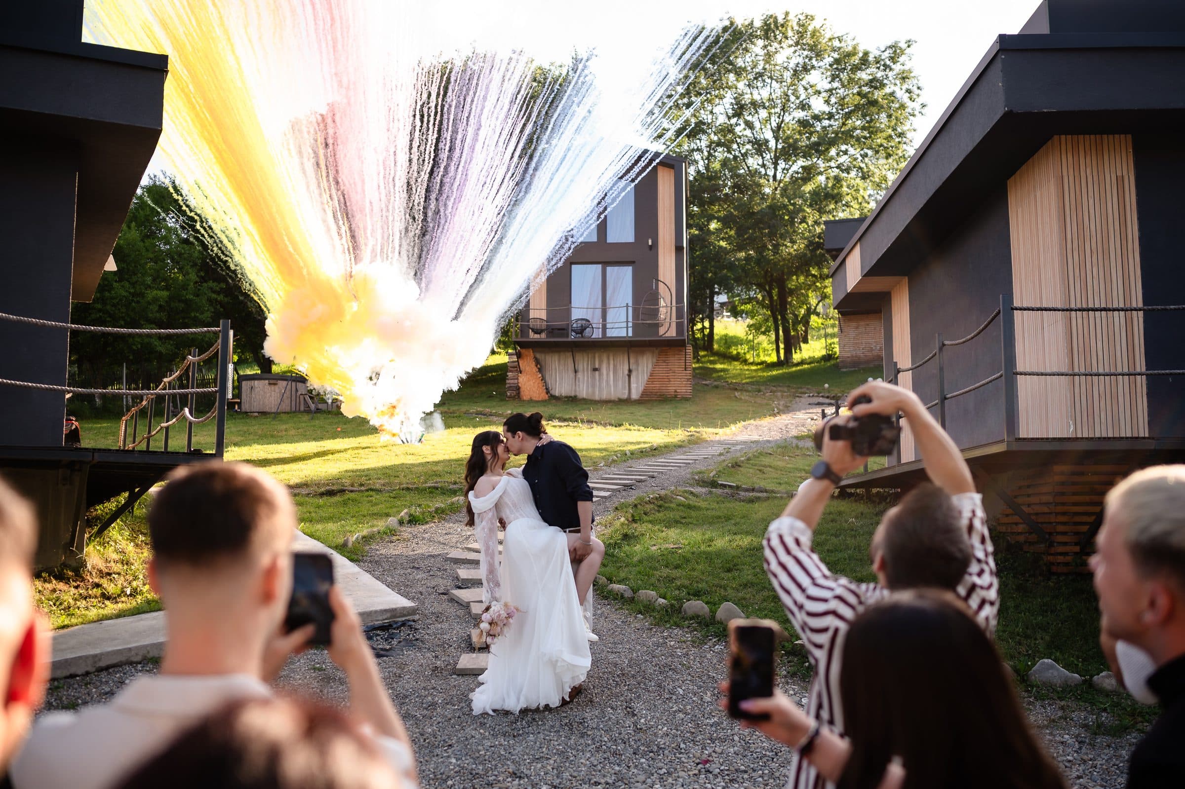 Coloured smoke rises behind the kissing couple while guests film on their phones