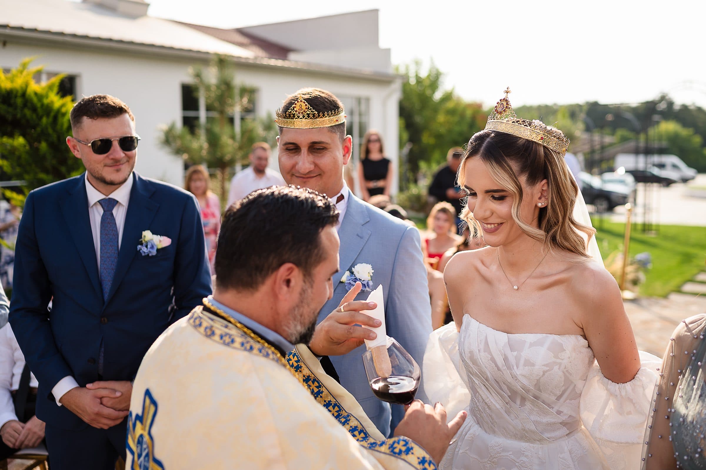 Outdoor service: the priest offers wine to the crowned couple as guests look on