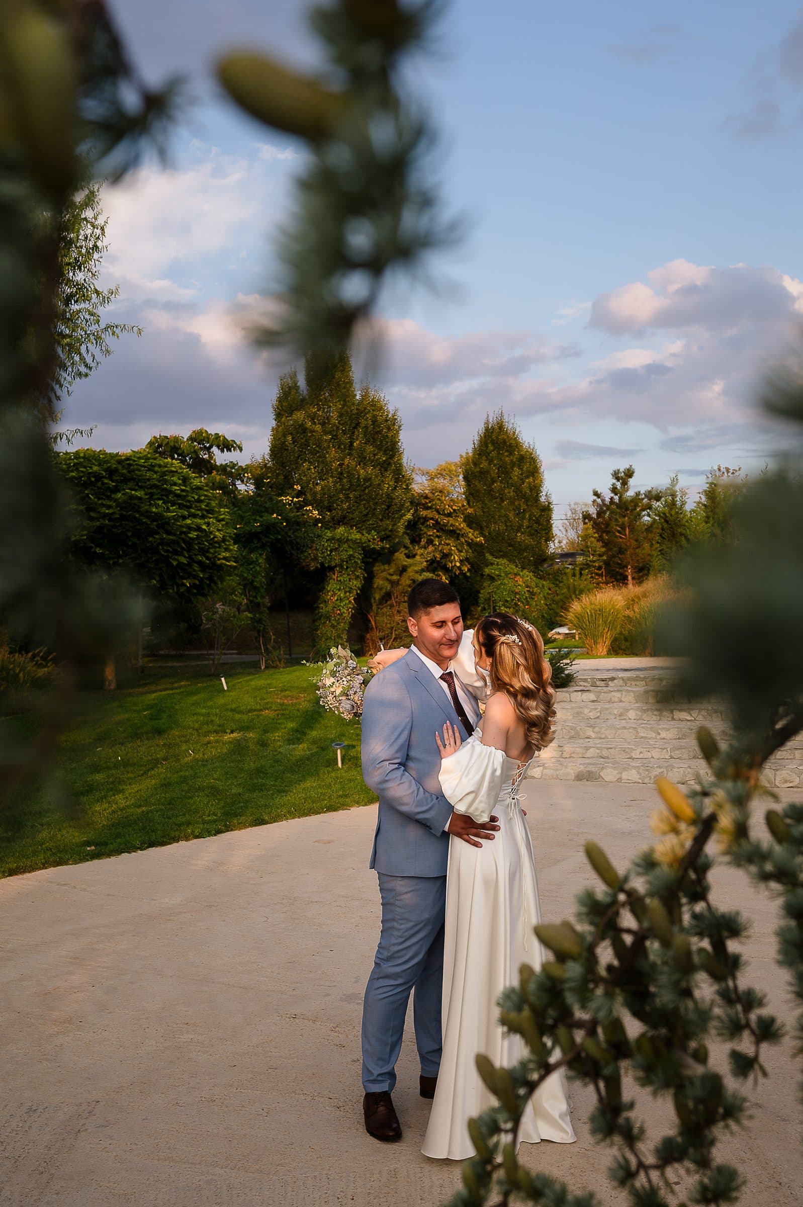 The groom kisses the bride's temple, seen through pine branches