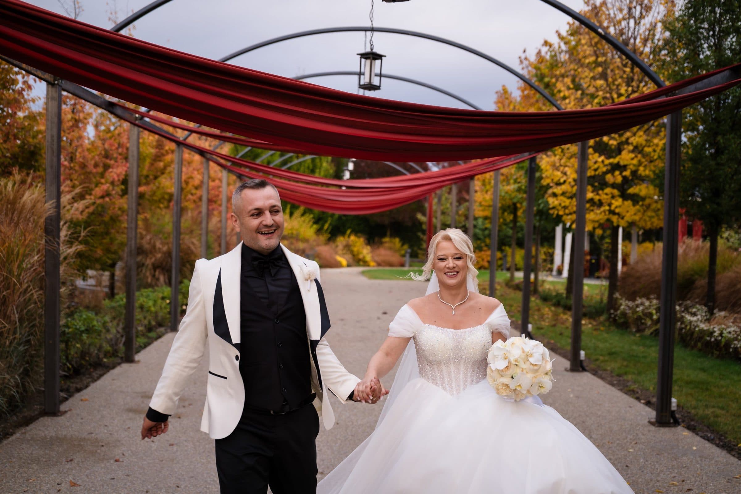 Bride and groom laughing as they walk hand in hand under red fabric arches