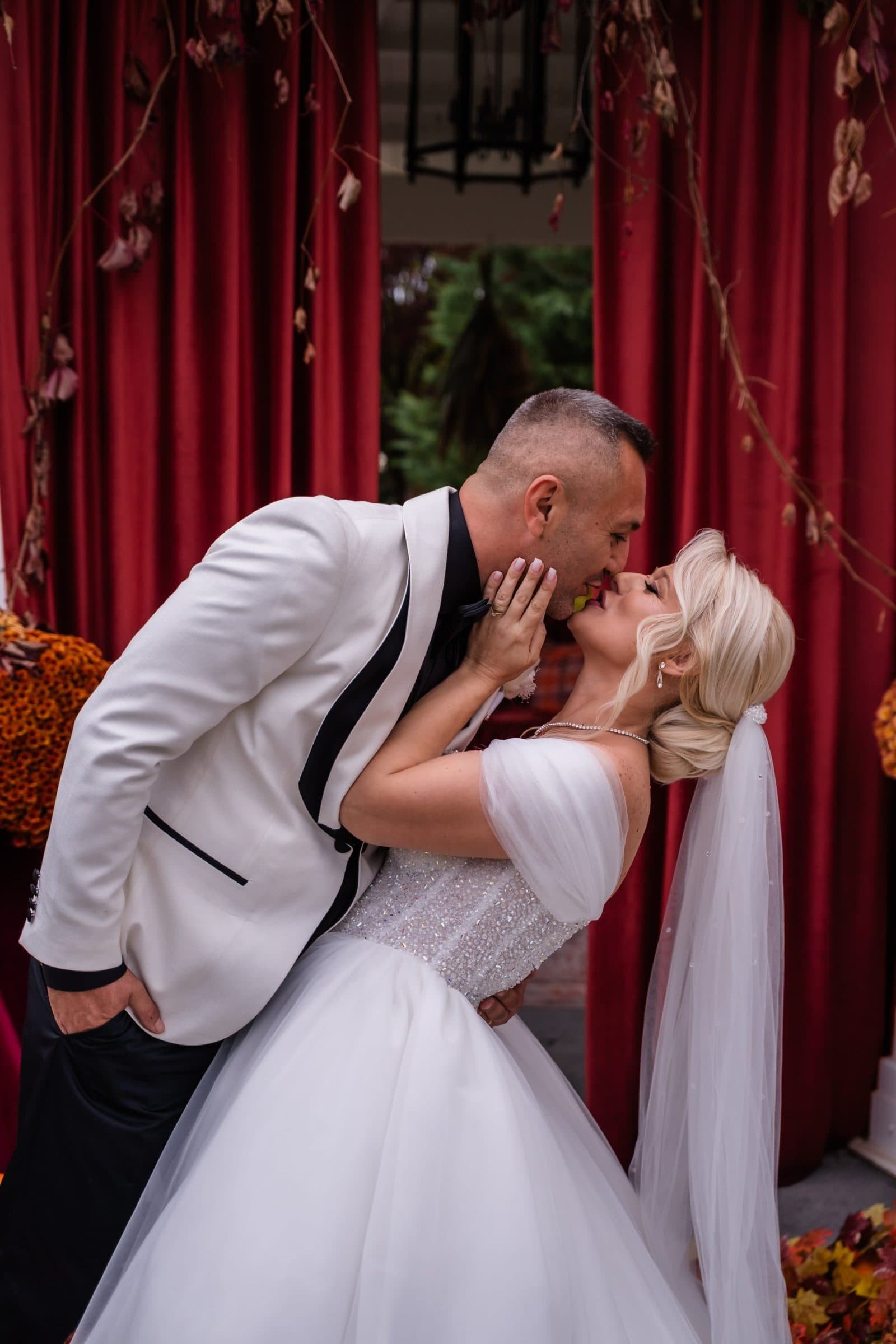 The groom dips the bride for a kiss in front of red velvet curtains
