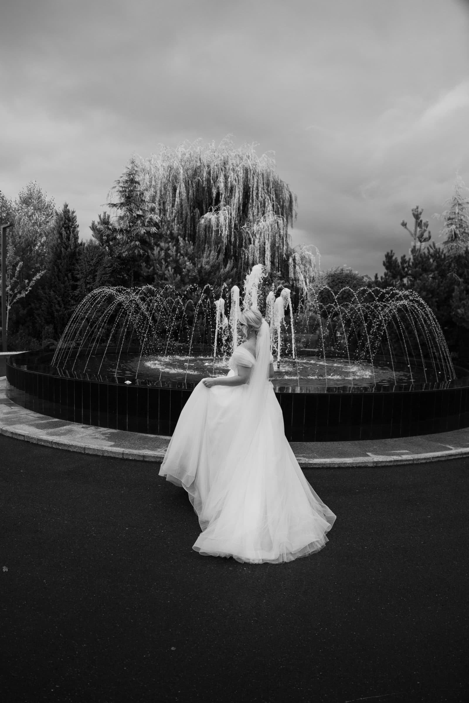 Black and white: the bride lifts her dress beside a fountain