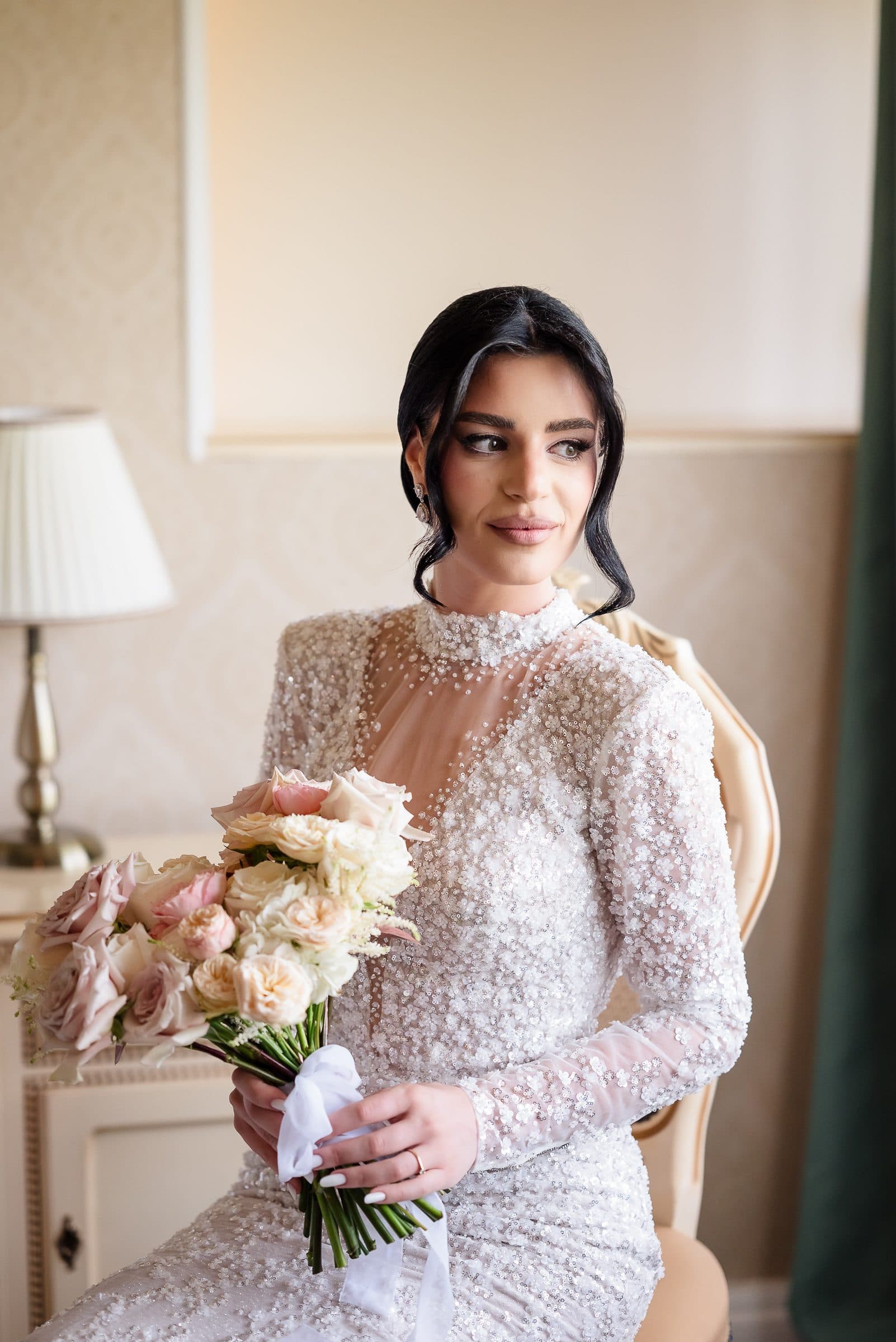 The bride glances toward the window, bouquet in her lap
