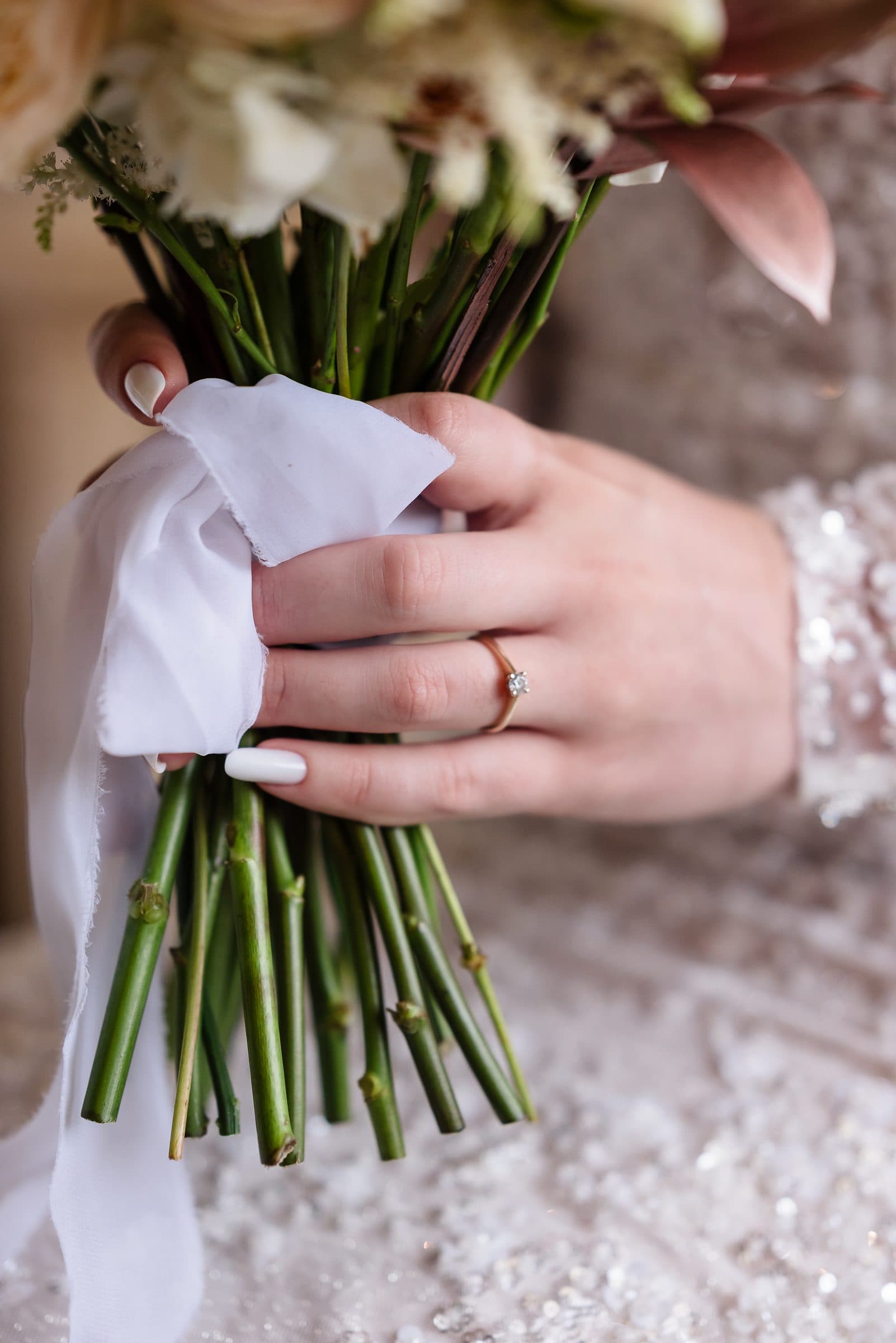 Detail: the bride's hand with her engagement ring, wrapped around the bouquet ribbon