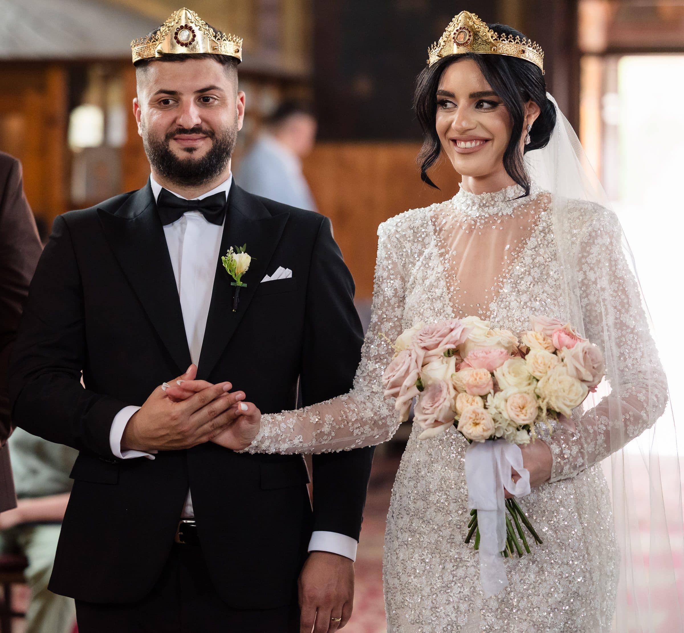 Bride and groom wearing wedding crowns during the church service, holding hands and smiling