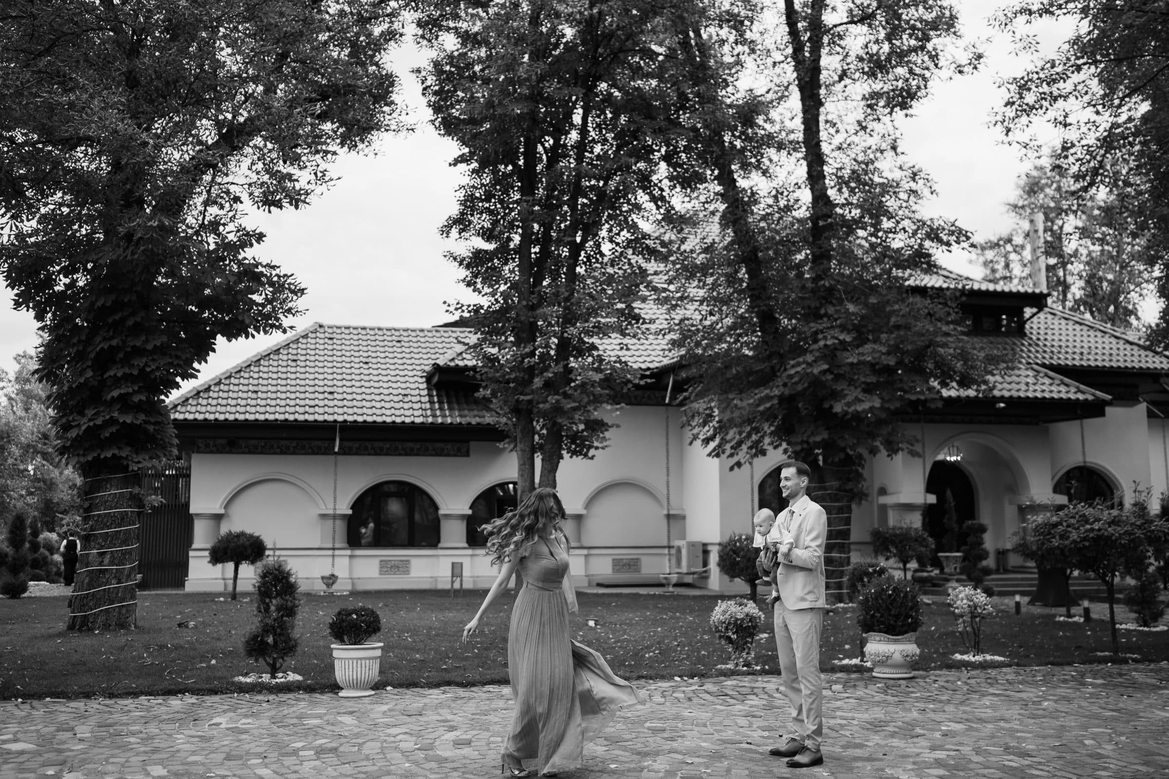 Black and white: the mother twirls in the garden while the father laughs, holding the baby